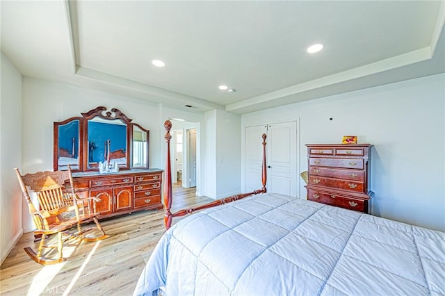 bedroom with a tray ceiling, light hardwood / wood-style flooring, and a closet