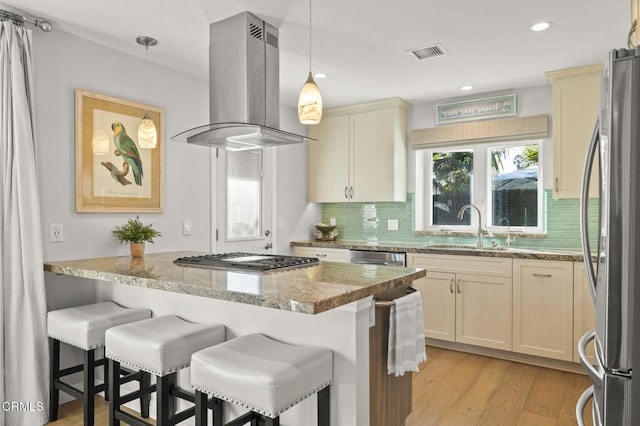 kitchen featuring stainless steel appliances, island range hood, pendant lighting, and light stone countertops