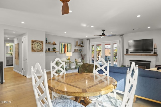 dining area with a brick fireplace, ceiling fan, and light hardwood / wood-style flooring