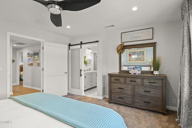 bedroom with a barn door, ceiling fan, light carpet, and ensuite bath