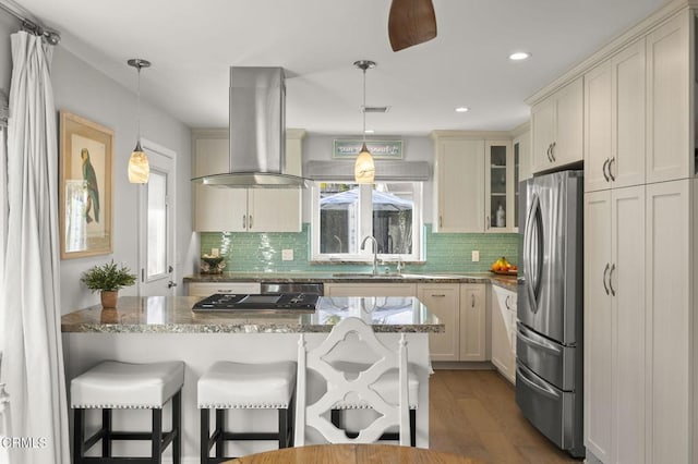 kitchen featuring island range hood, stainless steel appliances, light stone countertops, pendant lighting, and sink