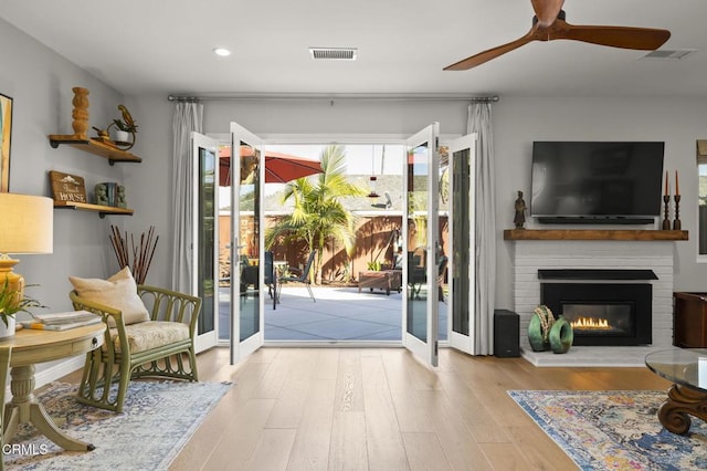 doorway featuring a large fireplace, french doors, ceiling fan, and light hardwood / wood-style flooring