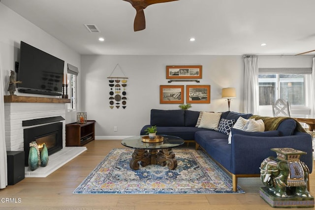 living room featuring a large fireplace, ceiling fan, and hardwood / wood-style flooring