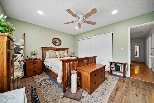 bedroom with a textured ceiling, light hardwood / wood-style floors, a closet, and ceiling fan