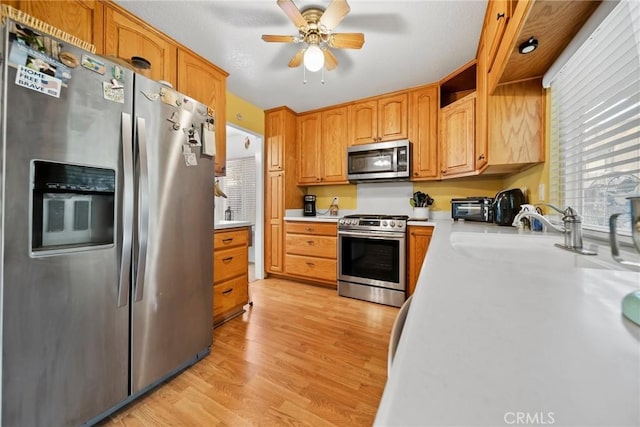 kitchen with stainless steel appliances, ceiling fan, sink, and light hardwood / wood-style floors