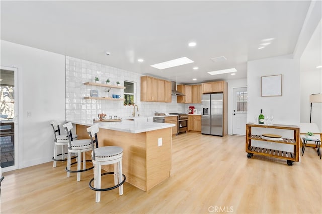 kitchen with a kitchen breakfast bar, appliances with stainless steel finishes, a skylight, kitchen peninsula, and light hardwood / wood-style flooring