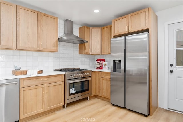 kitchen with stainless steel appliances, light brown cabinetry, wall chimney exhaust hood, and light hardwood / wood-style floors