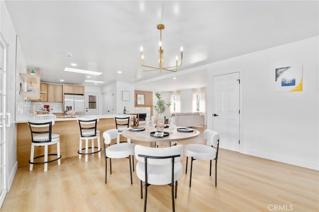 dining space featuring sink, light wood-type flooring, and a notable chandelier