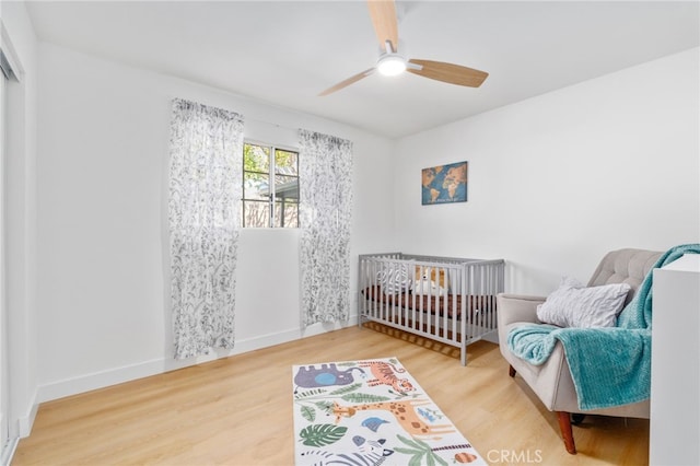 bedroom with ceiling fan, hardwood / wood-style floors, and a crib