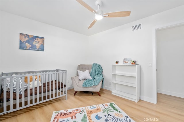 bedroom with ceiling fan, hardwood / wood-style floors, and a nursery area