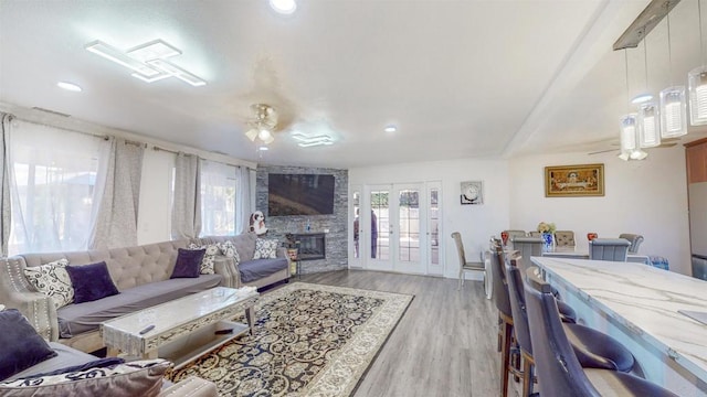 living area featuring light wood-type flooring, ceiling fan, a stone fireplace, and french doors