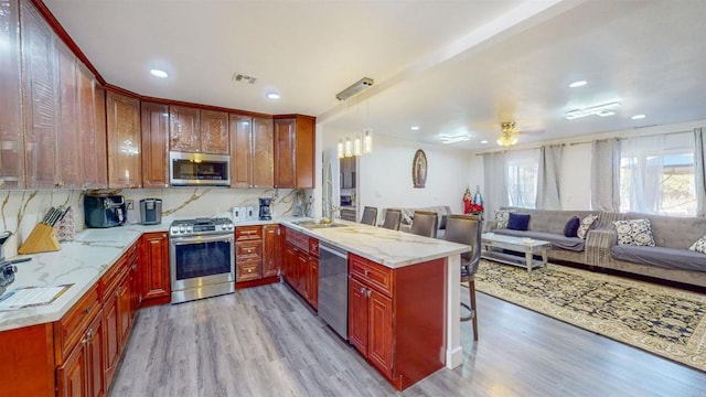 kitchen with visible vents, appliances with stainless steel finishes, open floor plan, a peninsula, and a sink