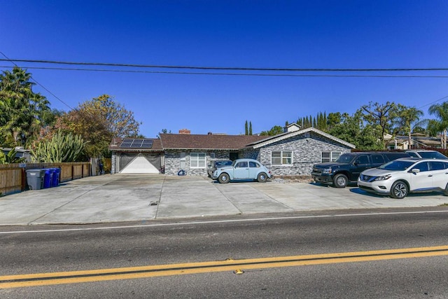 view of front facade with stone siding, roof mounted solar panels, fence, and concrete driveway