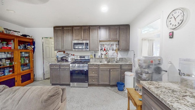 kitchen with stainless steel appliances, open floor plan, a sink, and light stone counters