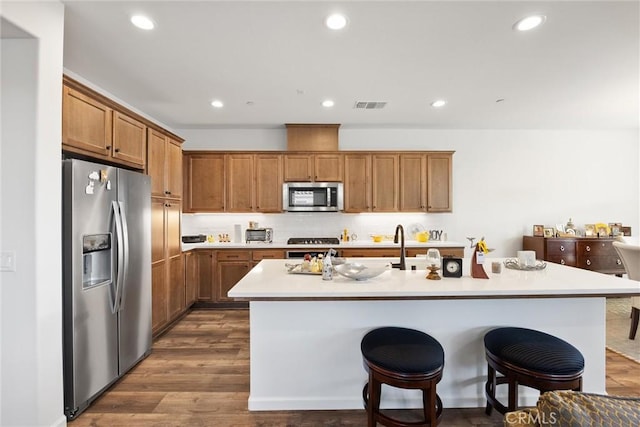 kitchen with a breakfast bar, appliances with stainless steel finishes, a center island with sink, and dark hardwood / wood-style flooring