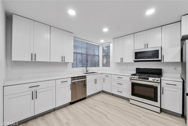 kitchen featuring stainless steel appliances, light stone countertops, white cabinets, light hardwood / wood-style flooring, and sink