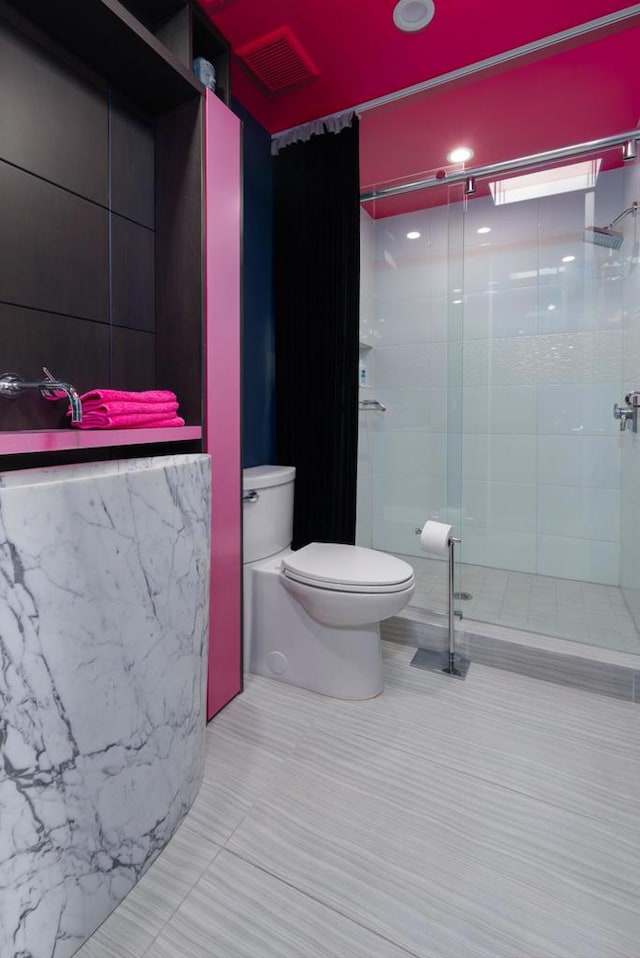 bathroom featuring toilet, a shower with door, and tile patterned floors