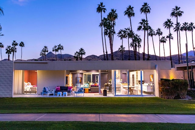 back house at dusk with a patio, a lawn, and a mountain view