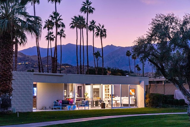 back house at dusk with a patio, a yard, and a mountain view