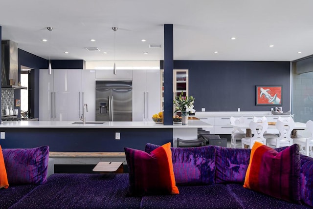 kitchen with sink, stainless steel built in fridge, white cabinetry, wall chimney exhaust hood, and hanging light fixtures