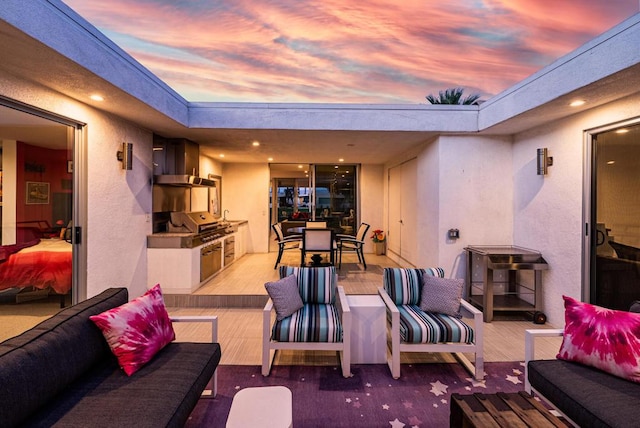 patio terrace at dusk featuring grilling area, exterior kitchen, and an outdoor living space