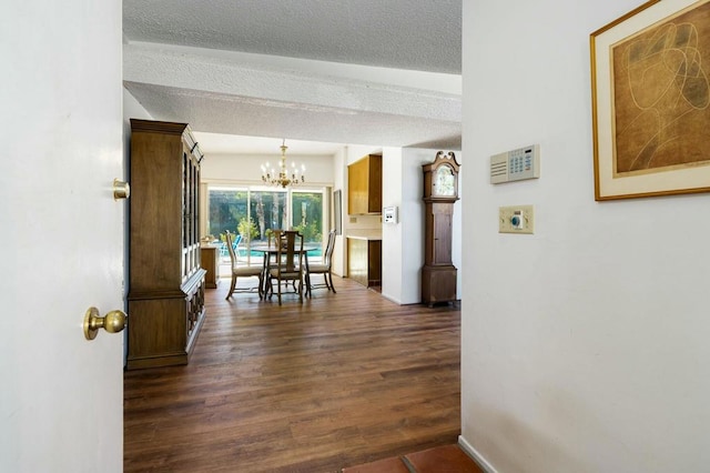 hallway with dark wood-type flooring, a textured ceiling, and a chandelier