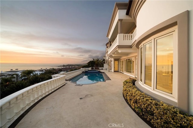 pool at dusk featuring a patio area and a water view