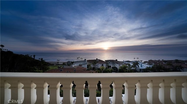 balcony at dusk featuring a water view