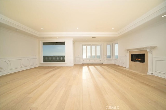 unfurnished living room featuring a raised ceiling, light hardwood / wood-style floors, a premium fireplace, and crown molding