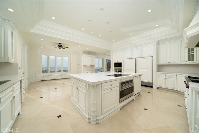 kitchen featuring stainless steel appliances, an island with sink, a raised ceiling, and white cabinets