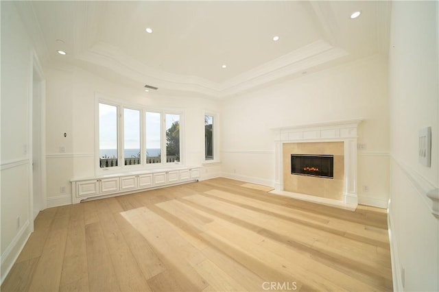 unfurnished living room featuring crown molding, a tray ceiling, and light hardwood / wood-style floors