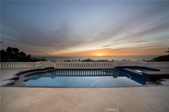 pool at dusk with a water view and a patio area