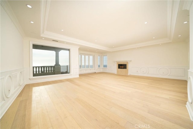 unfurnished living room with a tray ceiling, light hardwood / wood-style flooring, and crown molding