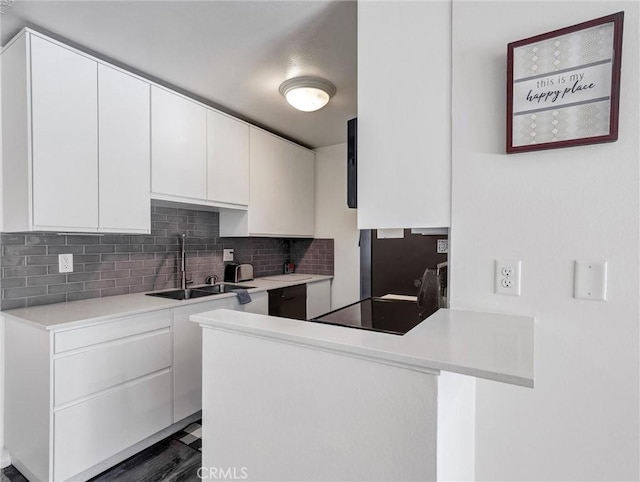 kitchen featuring a peninsula, a sink, white cabinets, light countertops, and tasteful backsplash