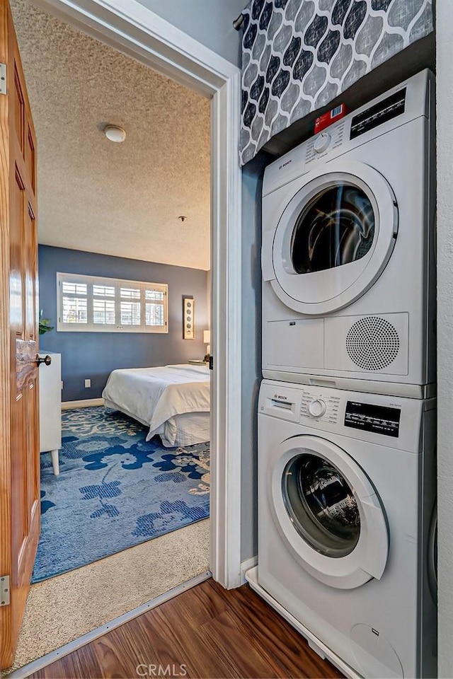 clothes washing area with a textured ceiling, stacked washer / drying machine, and dark hardwood / wood-style floors