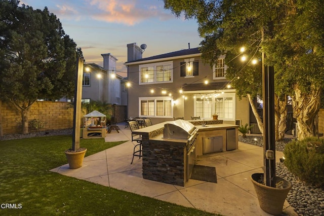 back house at dusk featuring a bar, a lawn, exterior kitchen, and a patio area