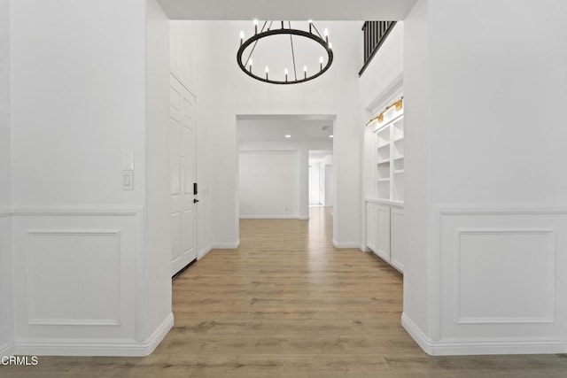 hallway featuring light hardwood / wood-style flooring, built in features, and an inviting chandelier