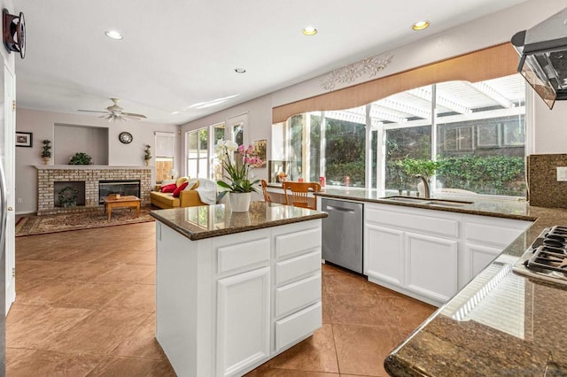 kitchen with dishwasher, a center island, a brick fireplace, sink, and white cabinetry