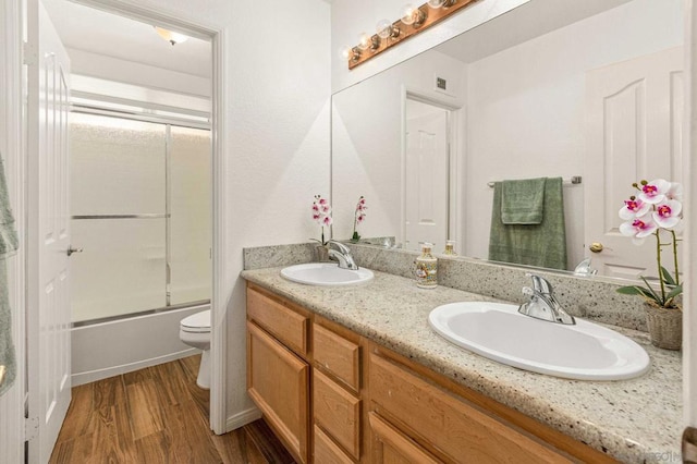 full bathroom with hardwood / wood-style floors, shower / bath combination with glass door, vanity, and toilet