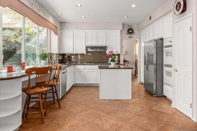 kitchen with stainless steel appliances, sink, white cabinetry, tasteful backsplash, and a kitchen island