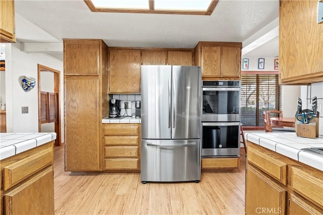 kitchen featuring light wood-type flooring, stainless steel appliances, tile countertops, and tasteful backsplash