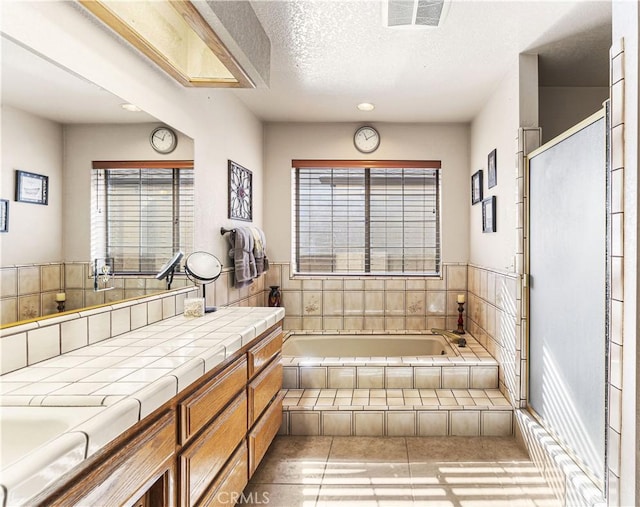 bathroom featuring a textured ceiling, tile patterned flooring, tiled bath, and vanity