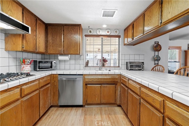 kitchen featuring tile countertops, range hood, decorative backsplash, light hardwood / wood-style flooring, and stainless steel appliances