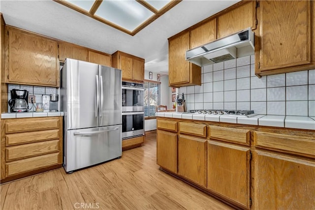 kitchen featuring decorative backsplash, appliances with stainless steel finishes, tile countertops, and light wood-type flooring