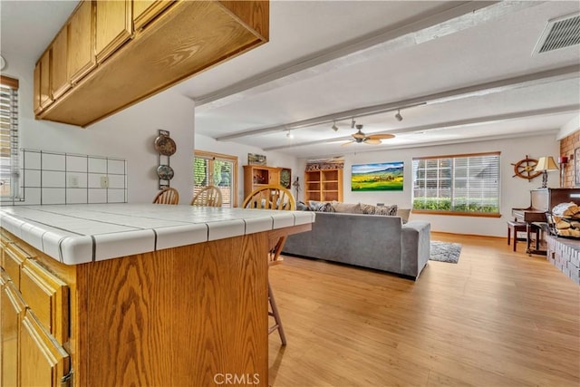 kitchen featuring light hardwood / wood-style floors, ceiling fan, tile counters, a breakfast bar area, and beam ceiling