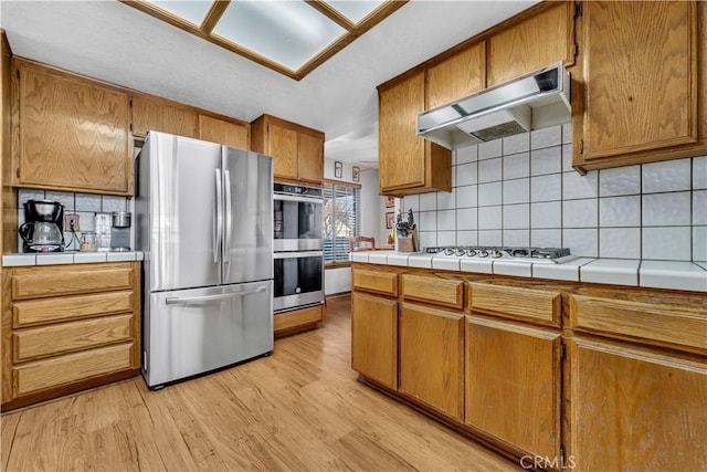 kitchen with light hardwood / wood-style floors, backsplash, stainless steel appliances, and tile countertops