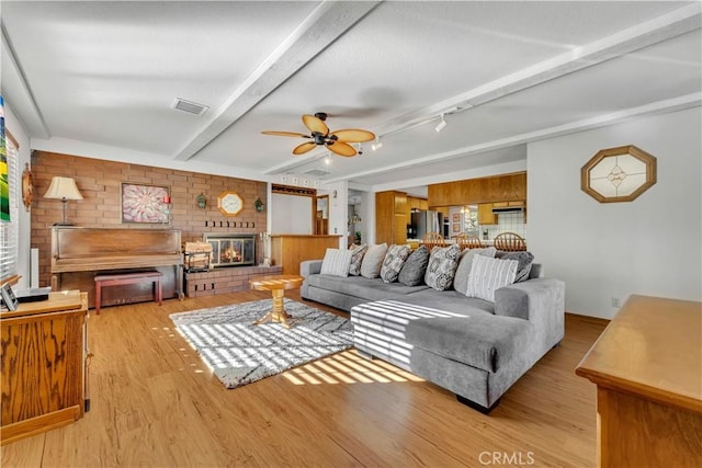 living room featuring light wood-type flooring, ceiling fan, a fireplace, and beamed ceiling