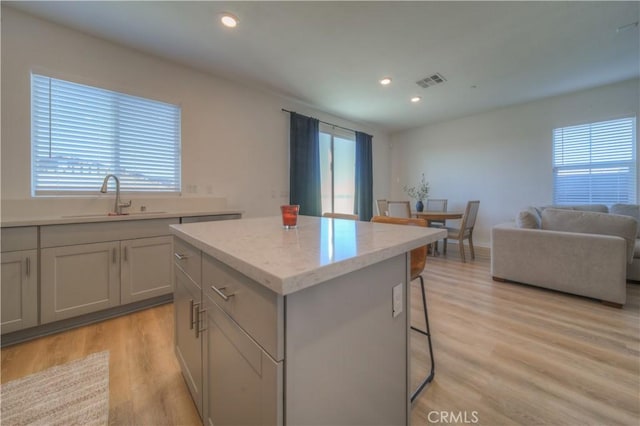 kitchen with light hardwood / wood-style floors, a breakfast bar, a kitchen island, gray cabinetry, and sink