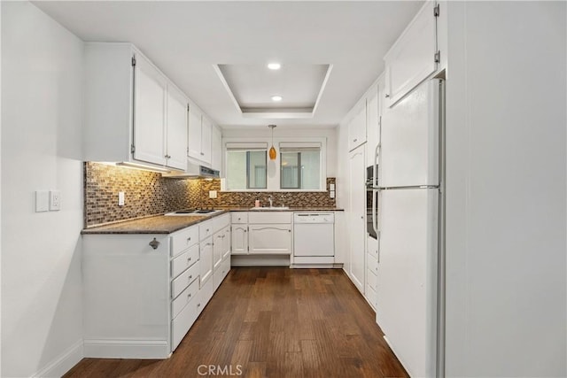 kitchen featuring white appliances, a raised ceiling, dark wood-type flooring, white cabinets, and decorative light fixtures