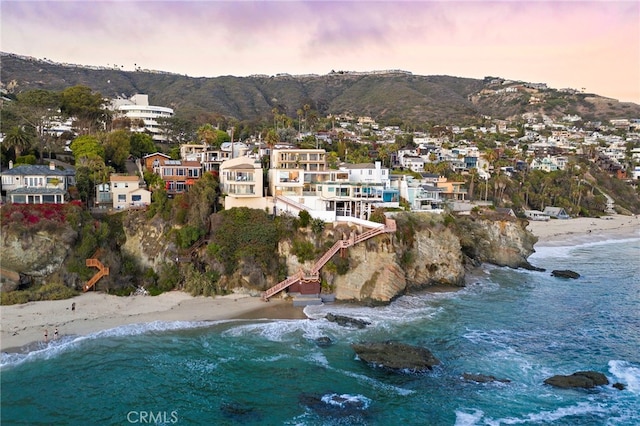 aerial view at dusk featuring a water and mountain view and a beach view